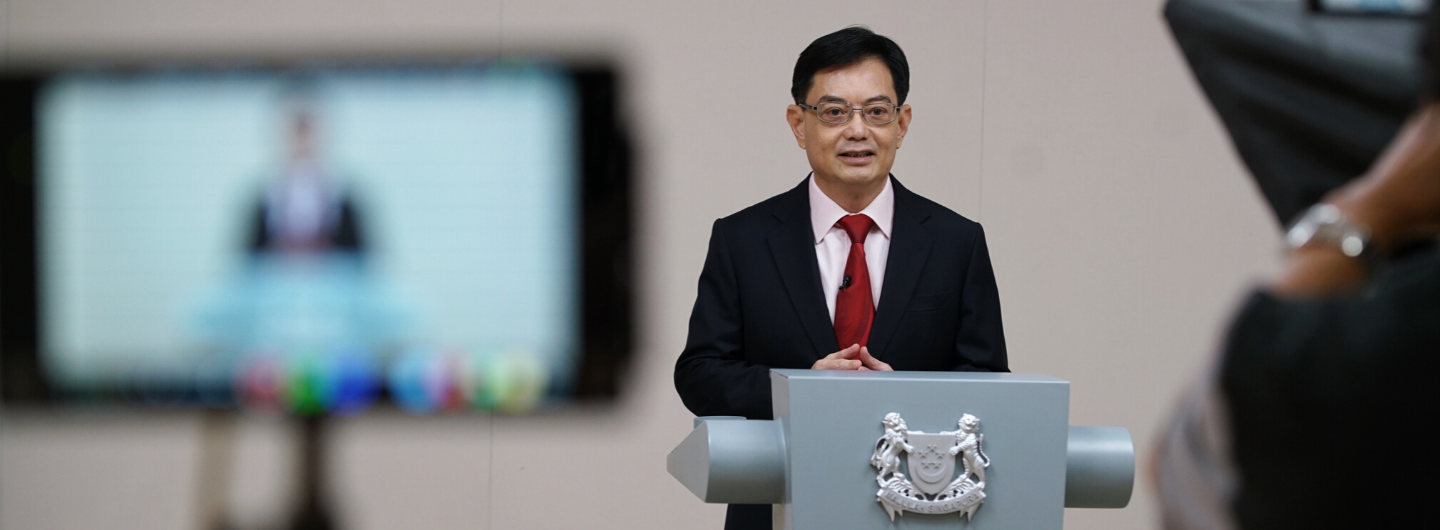 Man in suit behind podium with Singapore crest, blurred screen behind him.